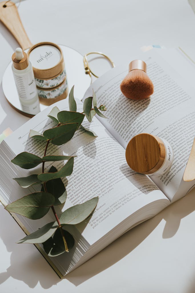 Chic flat lay of skincare products on an open book with green leaves.